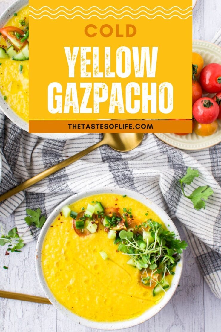 A bowl of Summer Yellow Gazpacho, topped with diced cucumber, herbs, and microgreens, sits on a white surface. Nearby are golden spoons, fresh cilantro, and cherry tomatoes. Text overlay reads &ldquo;Cold Yellow Gazpacho.&rdquo;.