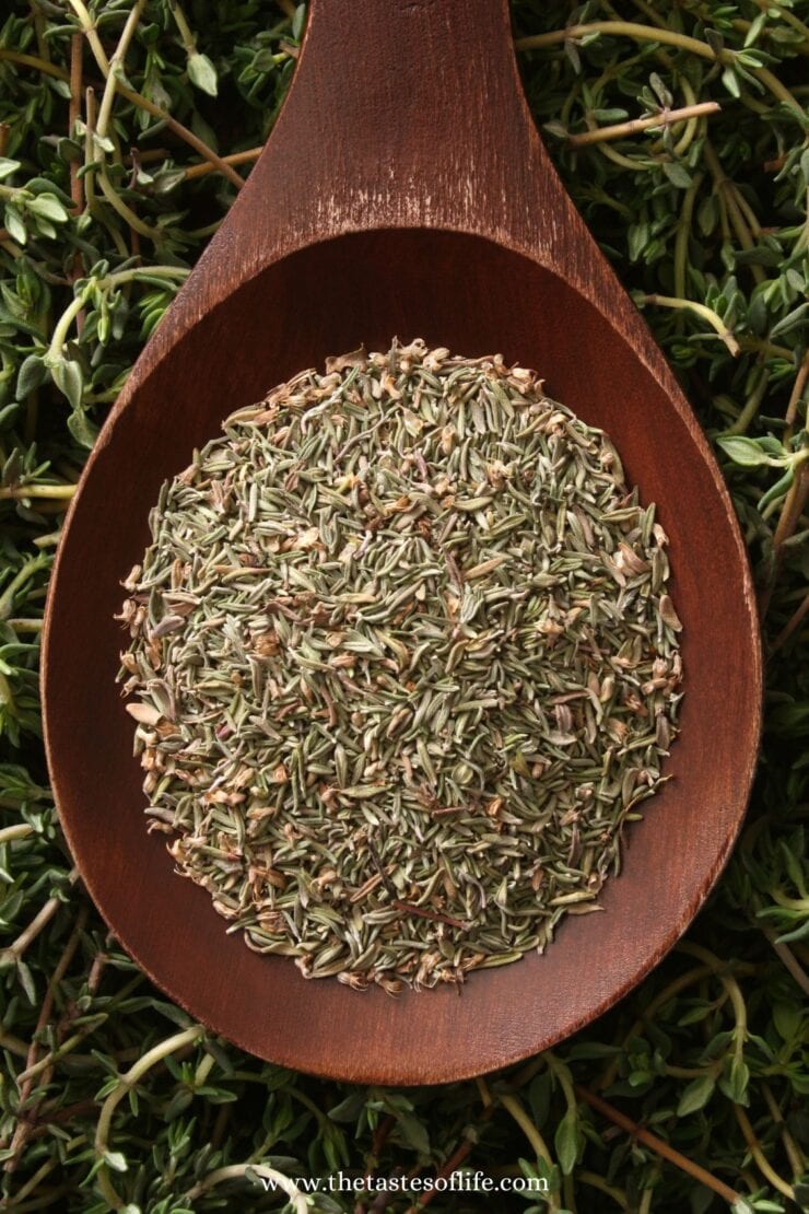 A wooden spoon filled with dried thyme leaves rests on a bed of fresh thyme sprigs.