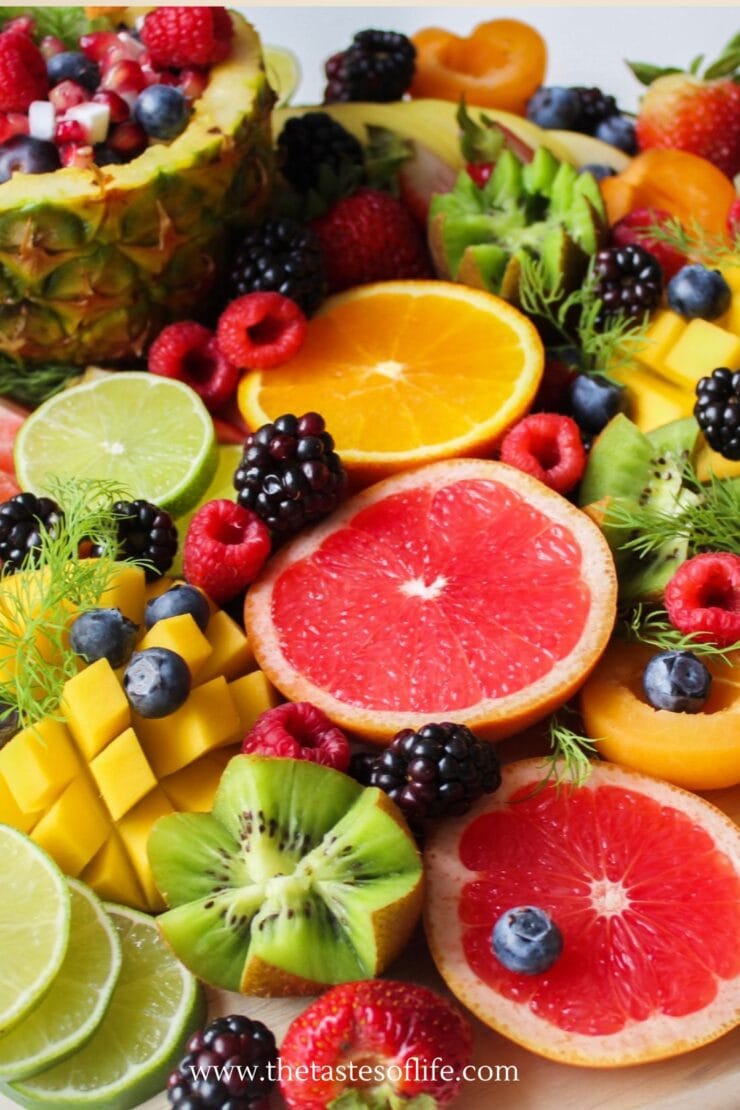 A colorful assortment of fresh fruits, including sliced grapefruit, orange, lime, kiwi, mango, berries, and a pineapple bowl filled with fruit salad, arranged on a platter.