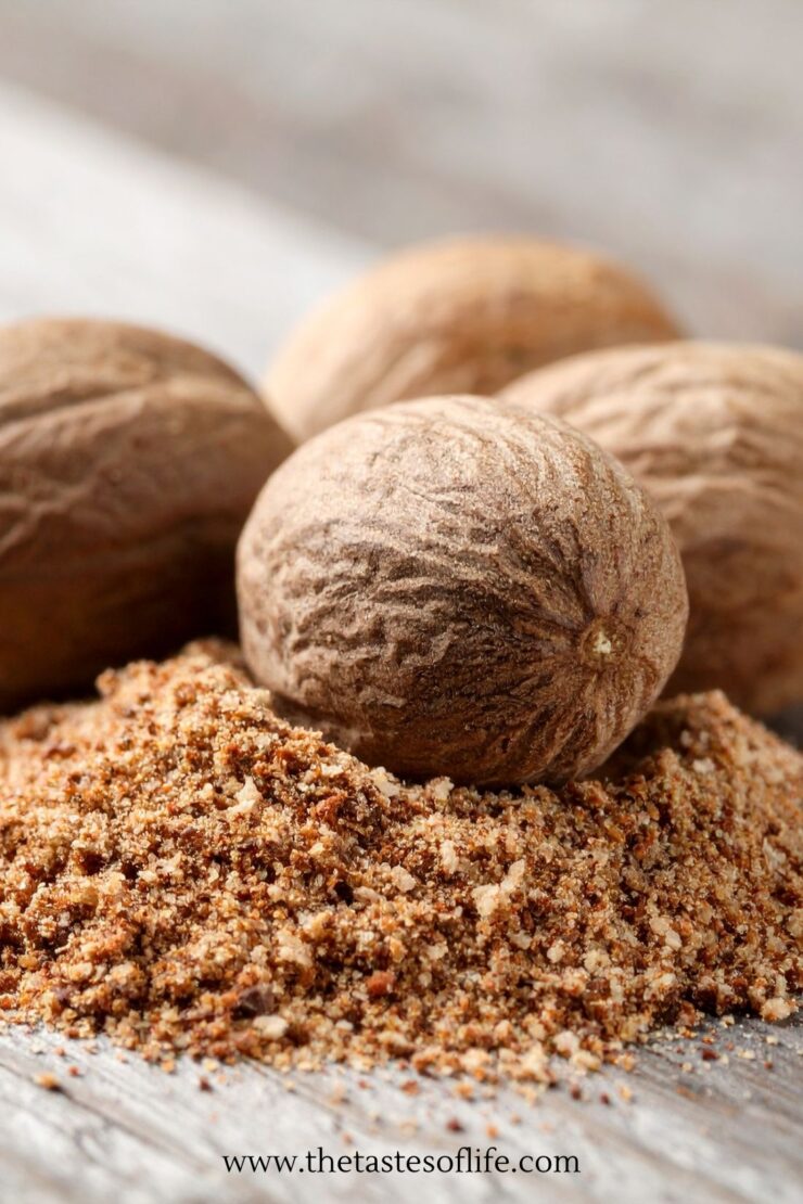 Whole nutmegs with a pile of ground nutmeg on a wooden surface. The image highlights the texture and color of both the whole and ground spice.