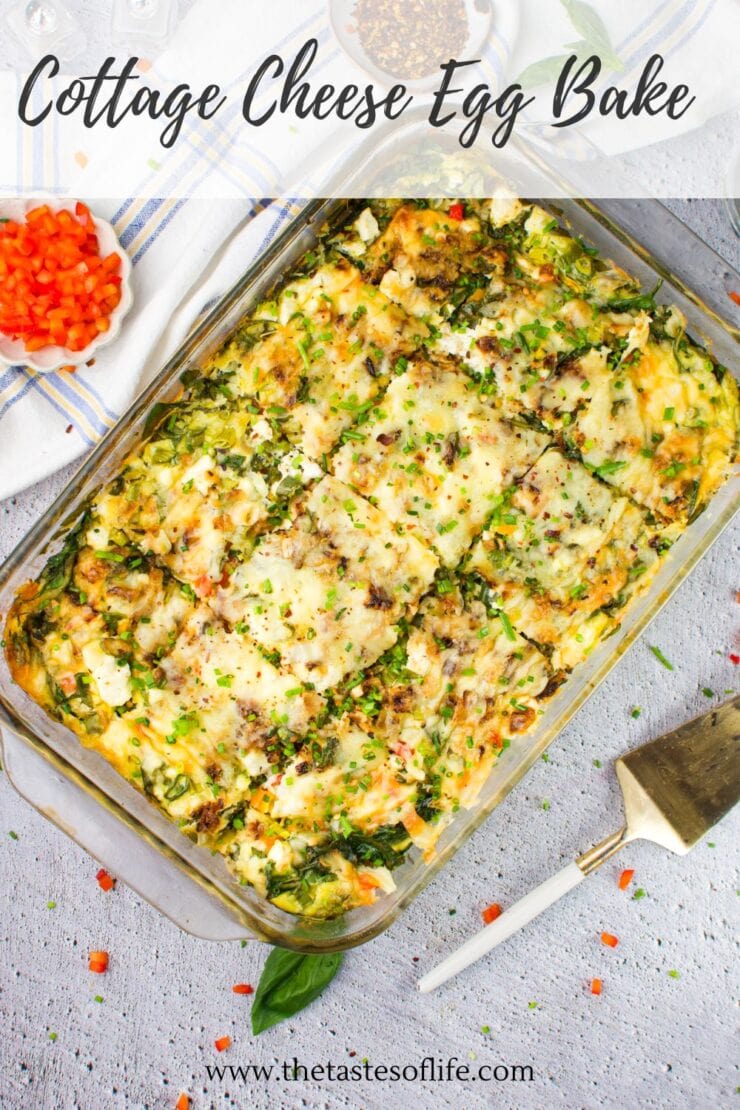 A glass baking dish filled with a golden, cheesy cottage cheese egg bake garnished with herbs, partially sliced. A spatula, chopped red bell peppers, and a striped napkin are visible nearby on a light surface.