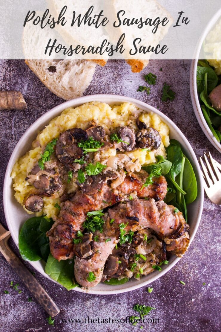A bowl filled with Polish white sausage in horseradish sauce, served over mashed potatoes with mushrooms and spinach, garnished with parsley. A slice of bread and a fork are beside the bowl.