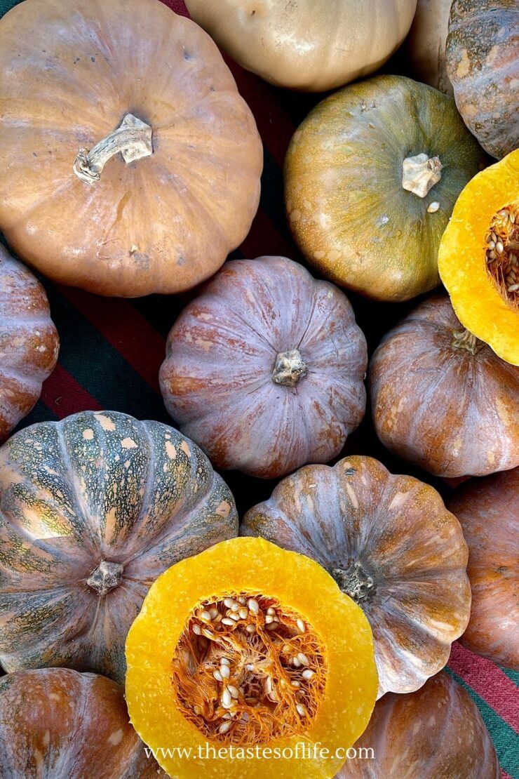 A collection of various pumpkins and squash, including a halved one showing its seeds, grouped together on a striped surface. The colors range from orange to green and tan.