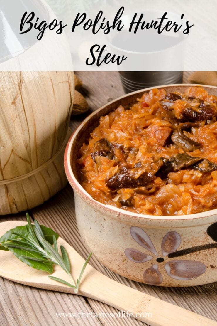 A ceramic bowl filled with Bigos Polish Hunters Stew, a hearty blend of cabbage, meat, and sausage, sits on a table next to a wooden spoon, bay leaf, and a rustic container.