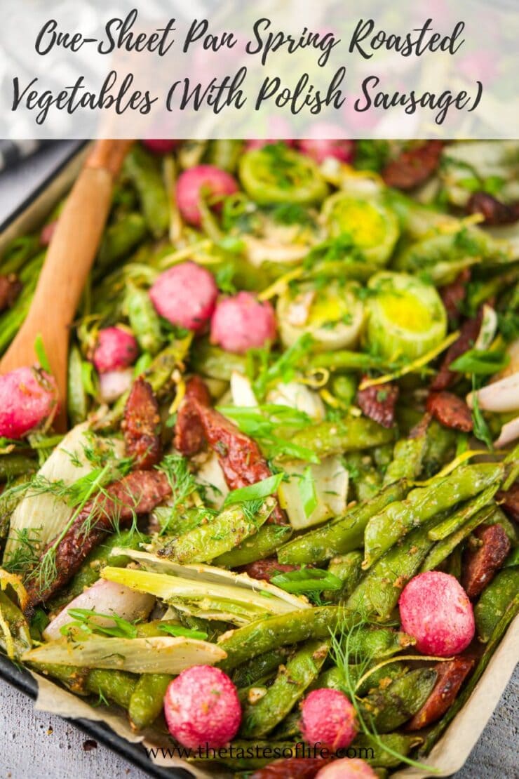 Close-up of a baking sheet filled with roasted spring vegetables, including asparagus, radishes, Brussels sprouts, and sliced Polish sausage, garnished with fresh herbs. A wooden spoon rests on the tray.