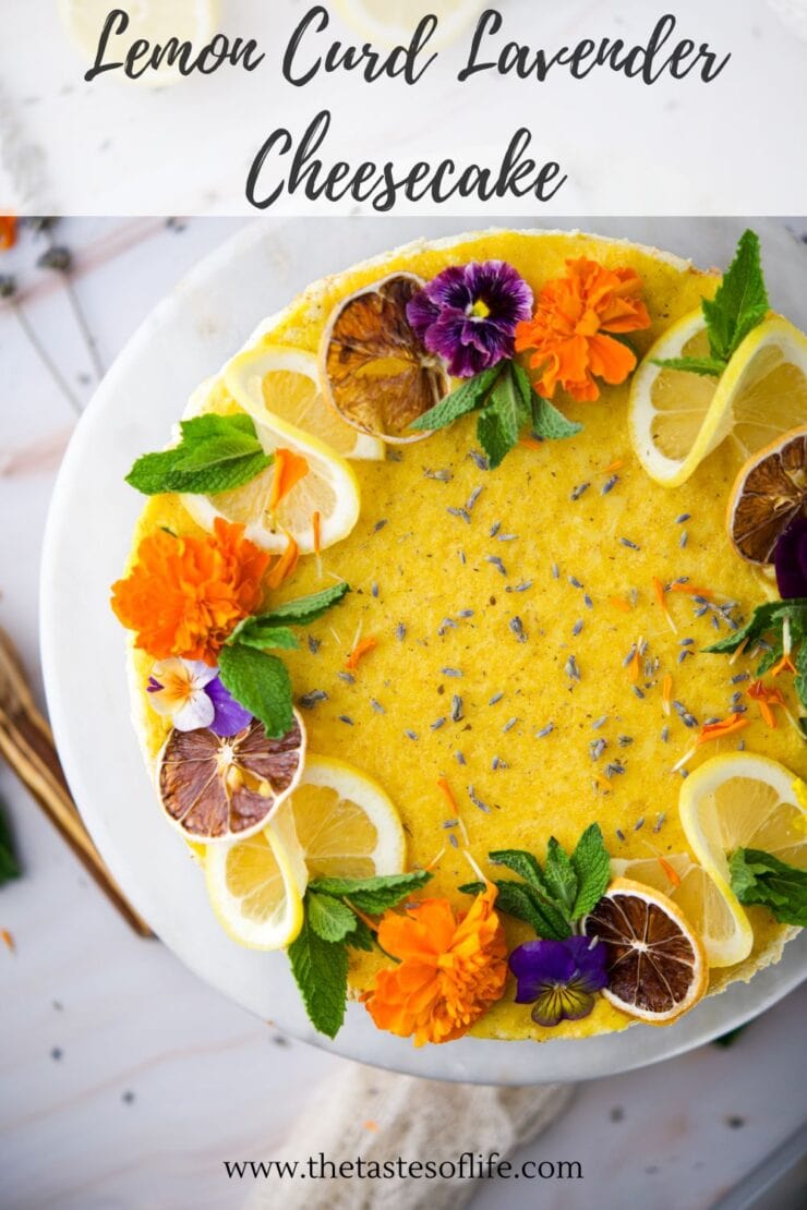 Top view of a lemon curd lavender cheesecake garnished with lemon slices, dried citrus, mint leaves, edible flowers, and lavender buds on a white plate. Text above reads Lemon Curd Lavender Cheesecake.