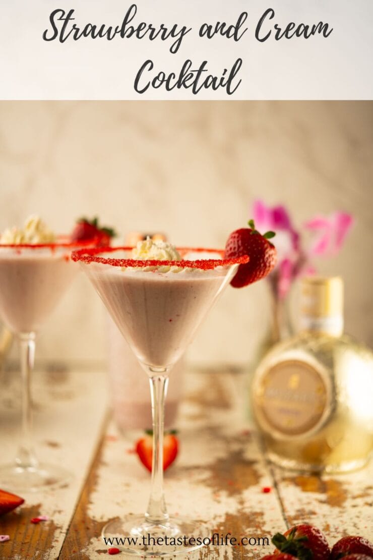 A strawberry and cream cocktail in a martini glass, garnished with a strawberry and a red sugar rim, sits on a rustic table with flowers and a bottle in the background. Text reads Strawberry and Cream Cocktail.