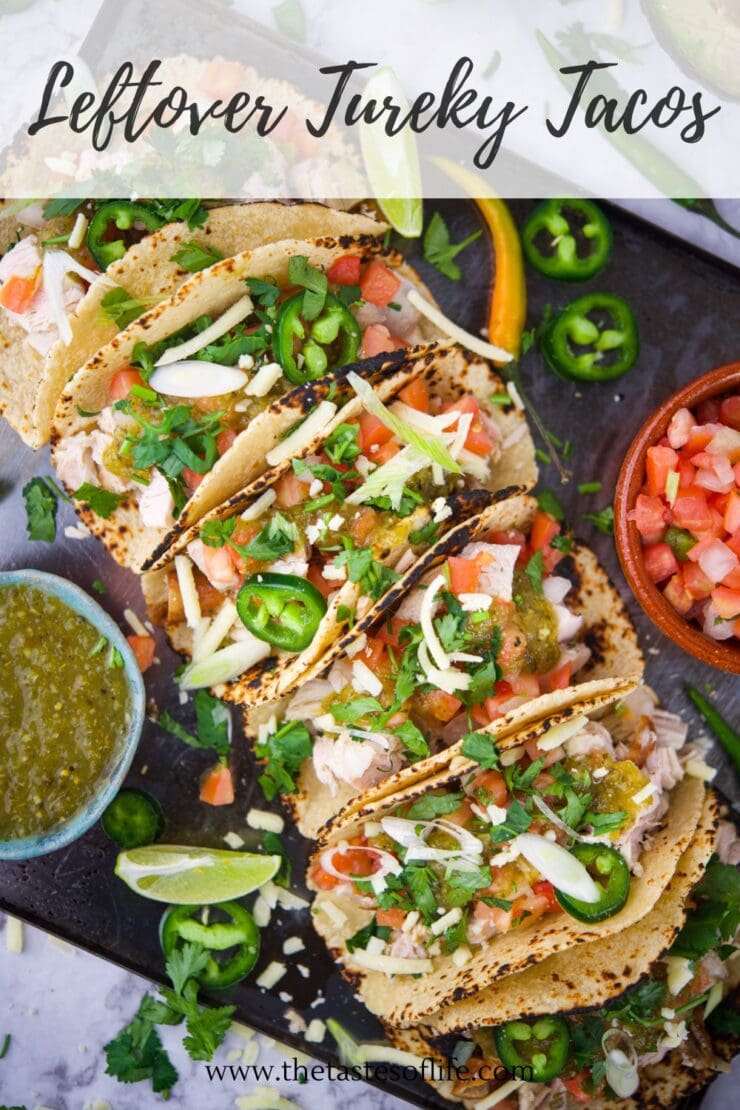 Four grilled tortillas filled with shredded turkey, salsa, jalapenos, cilantro, and cheese are arranged on a platter, with lime wedges, salsa verde, chopped onions, and pico de gallo on the side. Text reads Leftover Turkey Tacos.