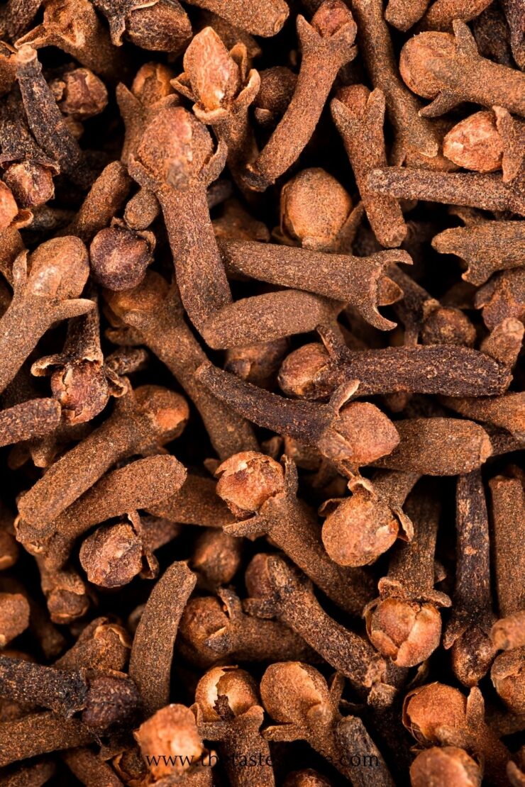 A close-up of dried whole cloves, showing their brown, woody stalks and rounded tops densely packed together.