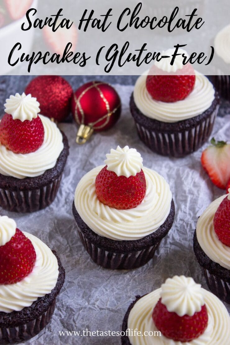 Chocolate cupcakes topped with white frosting and whole strawberries, arranged on parchment with red Christmas ornaments and sliced strawberries in the background. Text reads: Santa Hot Chocolate Cupcakes (Gluten-Free).