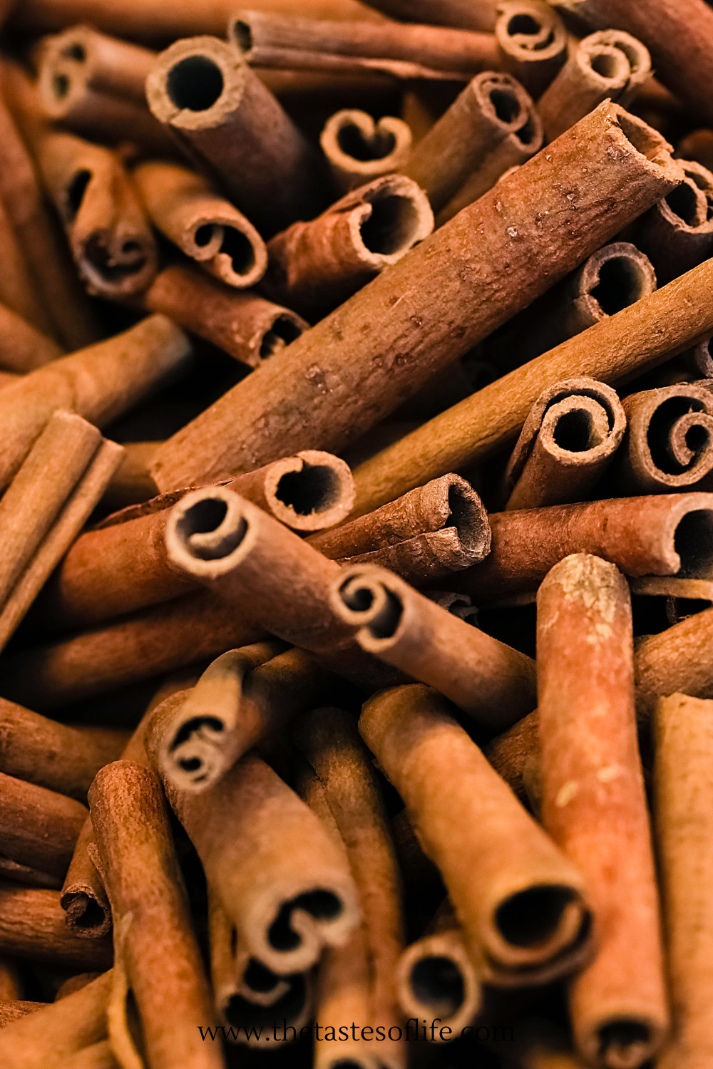 A close-up of several dried cinnamon sticks piled together, showing their curled, textured surfaces in warm brown tones.