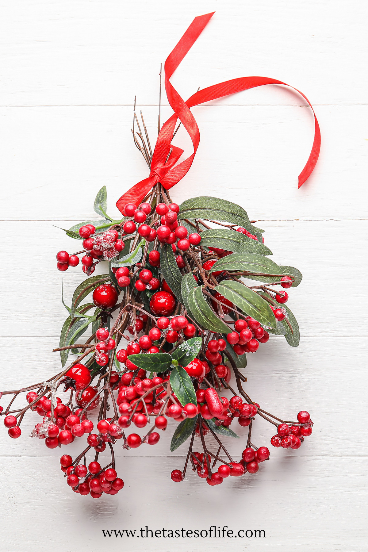 Artificial red berries and green leaves tied with a red ribbon against a white wooden surface, evocative of Slavic Christmas traditions.