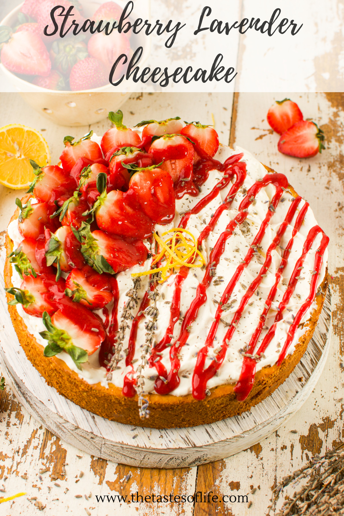 A cheesecake topped with fresh strawberries, lemon zest, and red sauce, with decorative chocolate shavings, sits on a distressed white wooden board. Strawberry Lavender Cheesecake is written above the dessert.