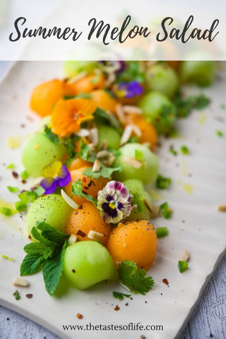 Colorful melon balls garnished with edible flowers, fresh mint, herbs, and chopped nuts, arranged on parchment paper with the text Summer Melon Salad at the top and thetasteoflife.com at the bottom.