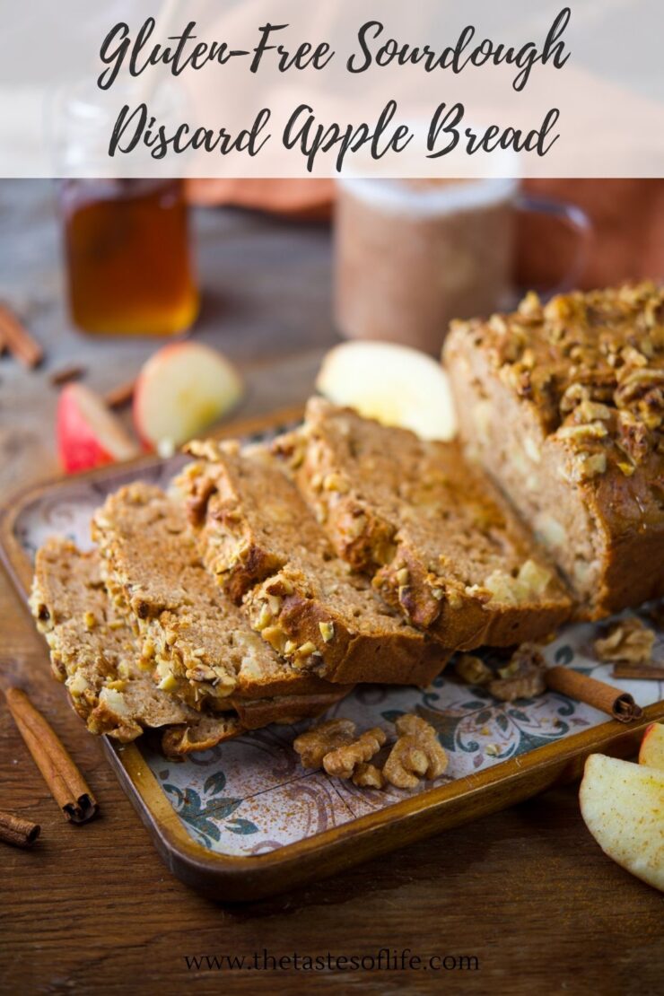 A sliced loaf of gluten-free sourdough apple bread with walnuts on a tray, surrounded by apple slices, cinnamon sticks, and jars on a wooden table. Text overlay reads Gluten-Free Sourdough Discard Apple Bread..