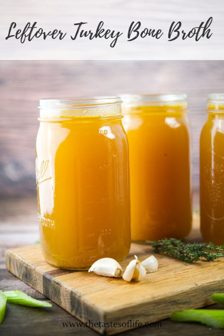 Three mason jars filled with golden turkey bone broth sit on a wooden board, accompanied by garlic cloves and fresh thyme, with the text Leftover Turkey Bone Broth above them.