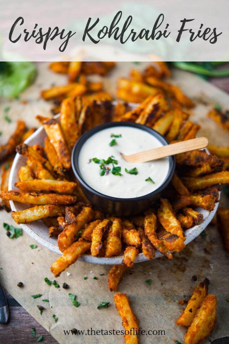 Bowl of golden, crispy kohlrabi fries with a creamy dipping sauce in the center, garnished with fresh herbs, on parchment paper. Text reads Crispy Kohlrabi Fries and www.thetastesoflife.com.