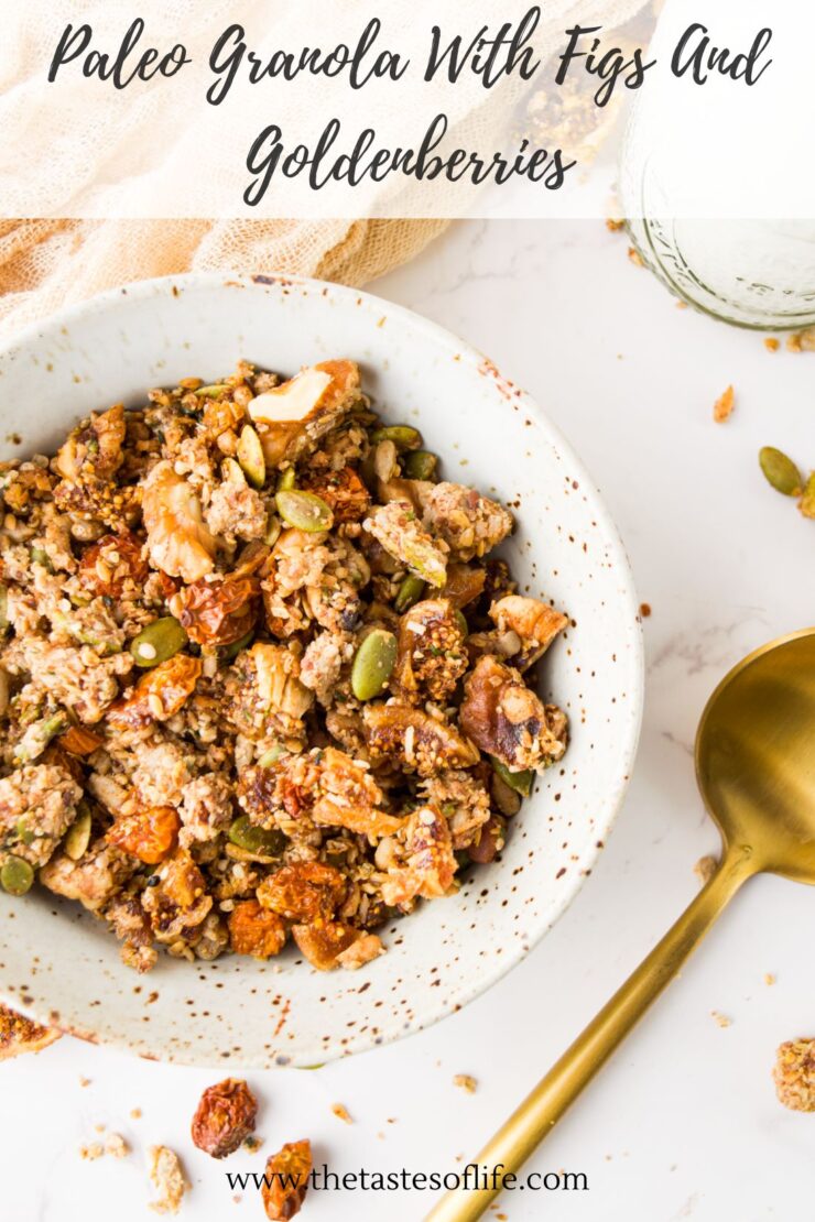 A bowl of paleo granola with figs and goldenberries sits on a white surface, surrounded by scattered granola pieces and a golden spoon. Text at the top reads, Paleo Granola With Figs And Goldenberries.