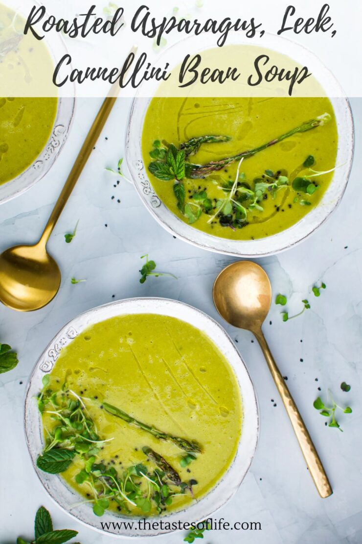 Three bowls of green roasted asparagus, leek, and cannellini bean soup, garnished with asparagus tips and fresh herbs, are shown on a light marble surface with gold spoons and herb sprigs beside them.