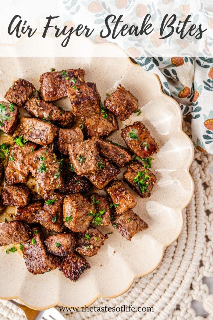 A plate of cooked steak bites garnished with chopped herbs, served on a scalloped dish. The text Air Fryer Steak Bites appears at the top, and a decorative napkin is partially visible beside the plate.