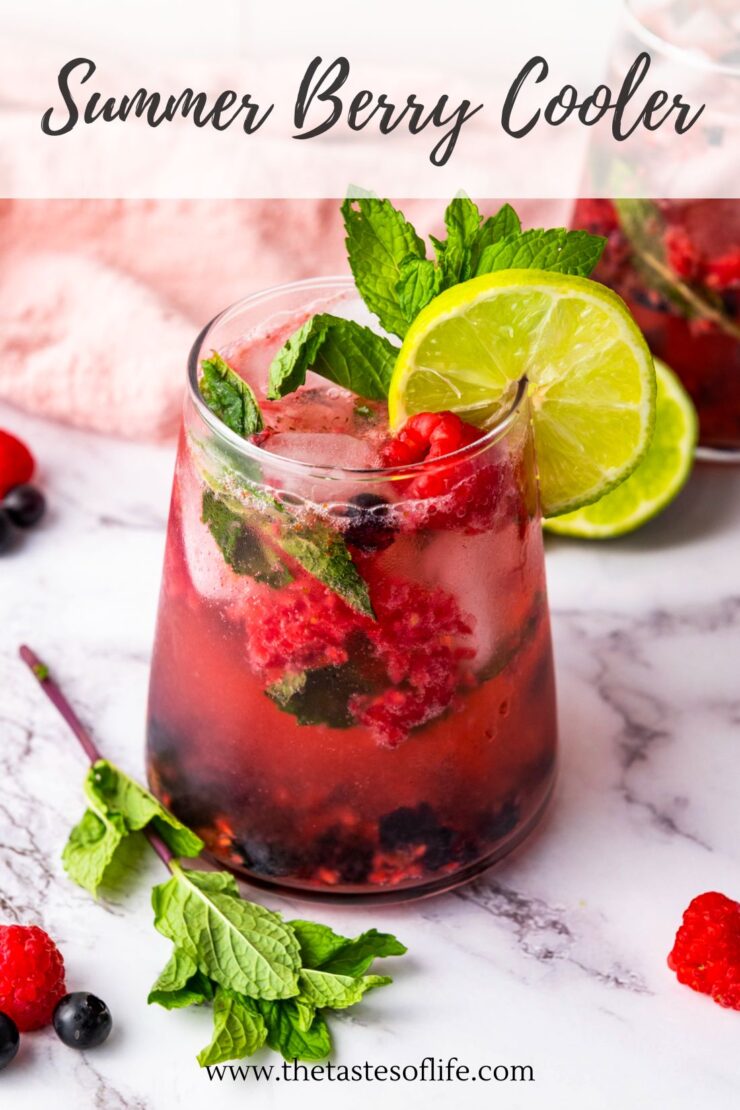 A glass of berry cooler with crushed ice, raspberries, blackberries, mint leaves, and lime slices, garnished with mint and lime. Marble surface and pink cloth in the background.