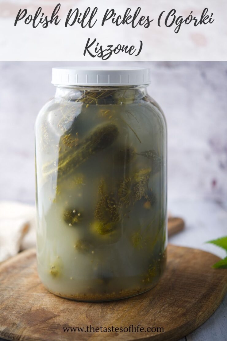 A large glass jar filled with homemade Polish dill pickles, sitting on a wooden surface. The label above reads Polish Dill Pickles (Og&oacute;rki Kiszone)..