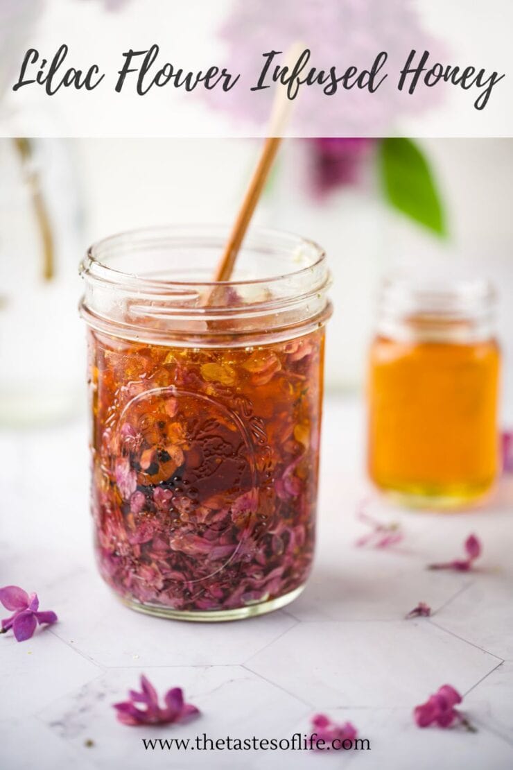 A glass jar filled with lilac flower-infused honey and a wooden dipper. Purple lilac petals are visible in the honey. There is a small jar of plain honey and lilac flowers in the background. Text reads Lilac Flower Infused Honey.