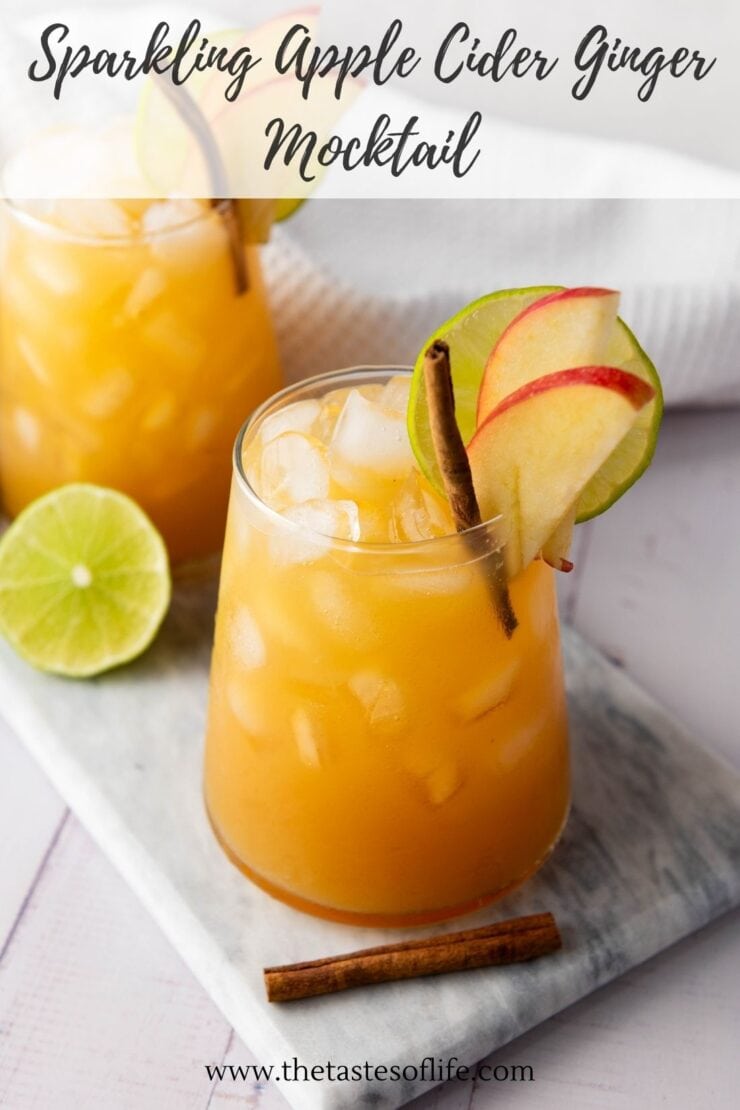 Two glasses of sparkling apple cider ginger mocktail with ice, apple slices, lime, and cinnamon sticks. A halved lime and a cinnamon stick sit nearby on a gray board. Handwritten text appears at the top of the image.