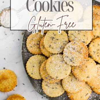 A plate of round lavender butter cookies sprinkled with powdered sugar sits on a white surface, with some cookies scattered around and lavender buds visible. Text reads: Lavender Butter Cookies Gluten-Free.