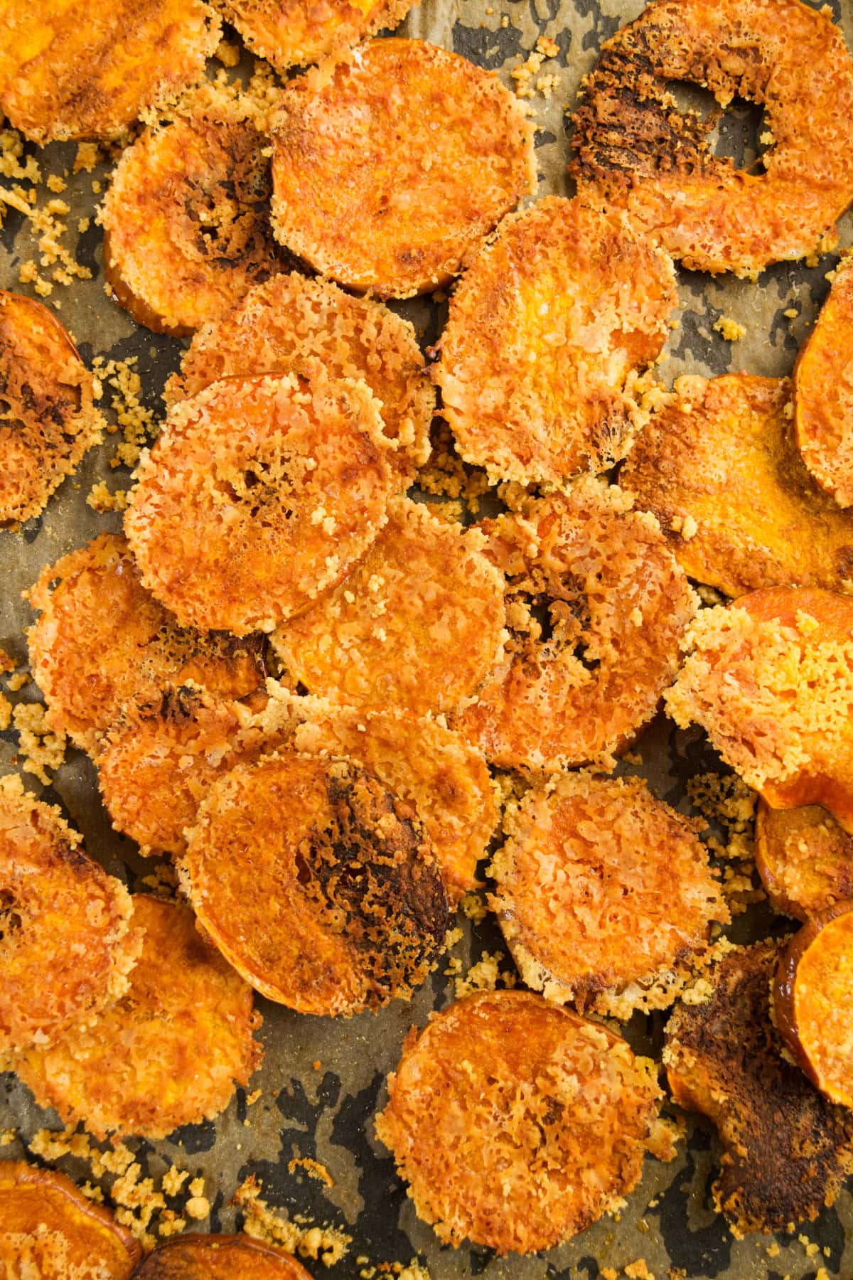 A close-up of crispy, golden-brown baked butternut squash and Parmesan chips coated with a layer of melted cheese and breadcrumbs on a baking sheet.