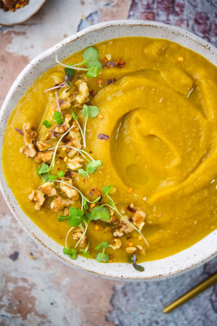 A bowl of roasted sweet potato pear soup topped with microgreens, chopped walnuts, and red pepper flakes.