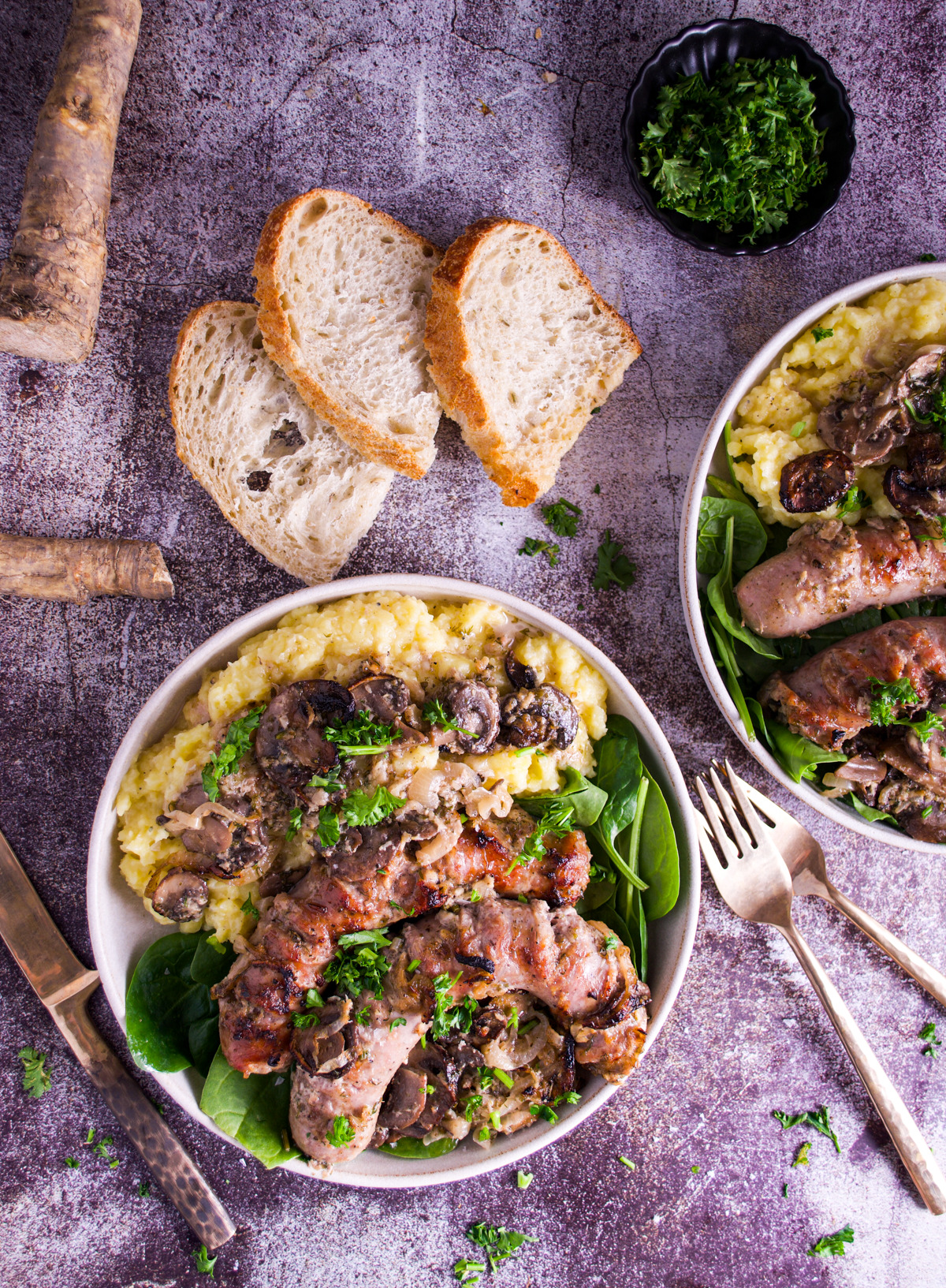 Two bowls of Polish White Sausage In Horseradish Sauce accompanied by two slices of rustic bread and a small bowl of chopped herbs.