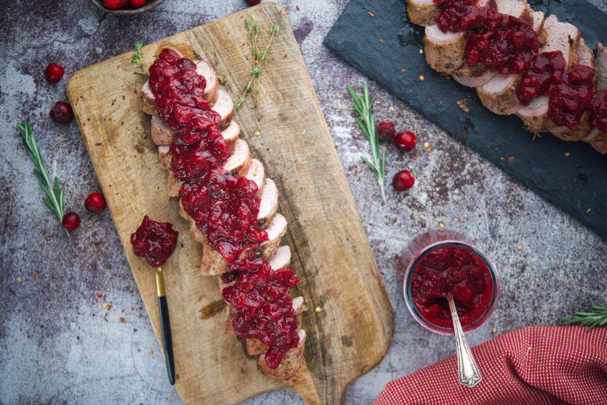Juicy pork tenderloin with cranberry sauce on a wooden cutting board.