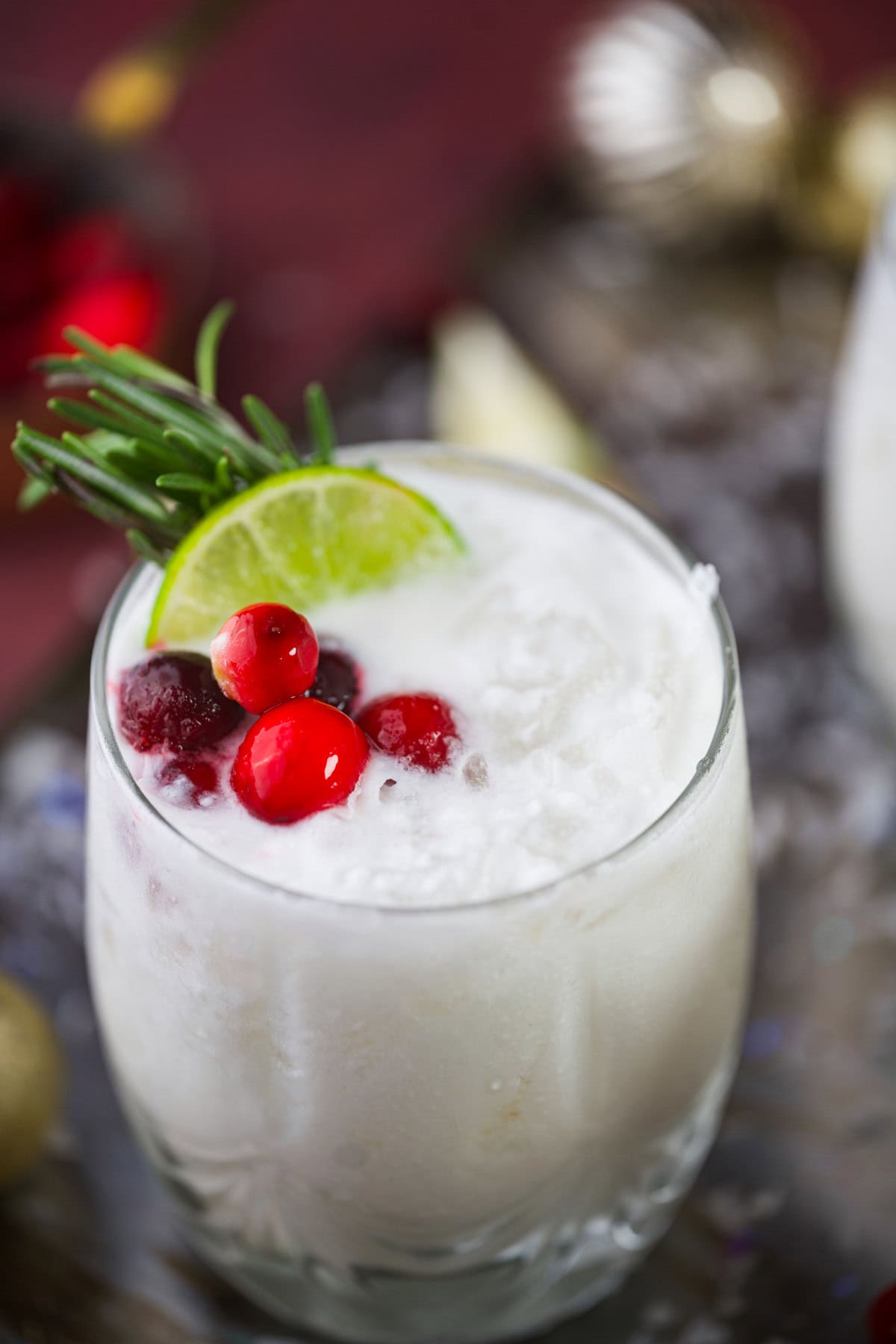 A creamy White Christmas Mezcal Cocktail garnished with a lime slice, cranberries, and a sprig of rosemary, served in a clear glass.