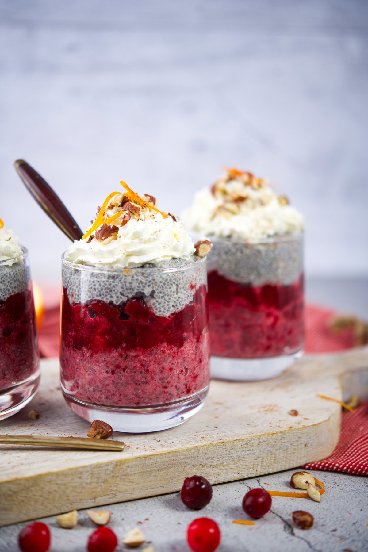 Fresh berry chia pudding parfait with whipped cream and nuts in glasses.