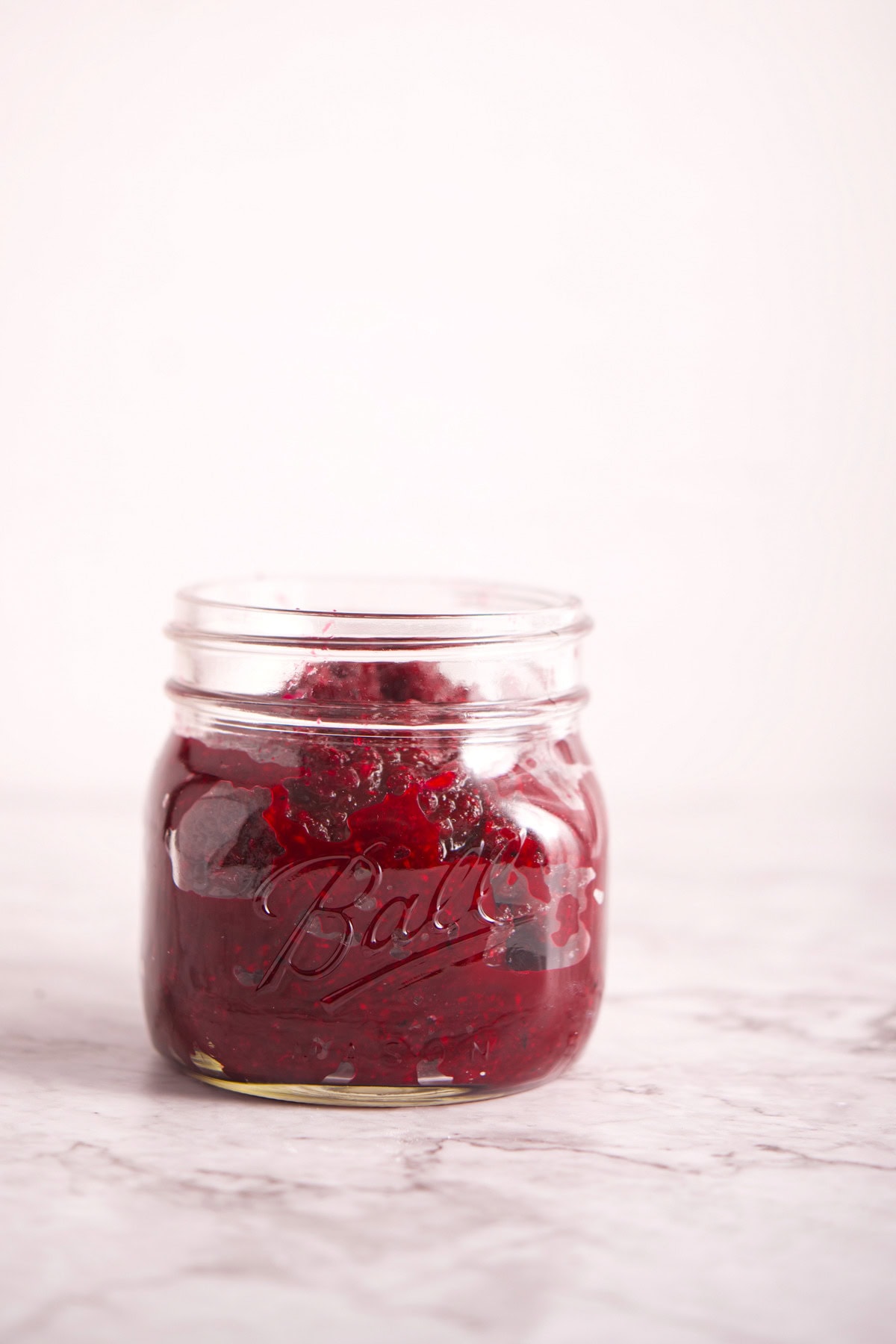 A small glass jar filled with Polish Beet and Horseradish (Ćwikła z Chrzanem) sits on a light marble surface against a plain white background. The jar has the word Ball embossed on the front.