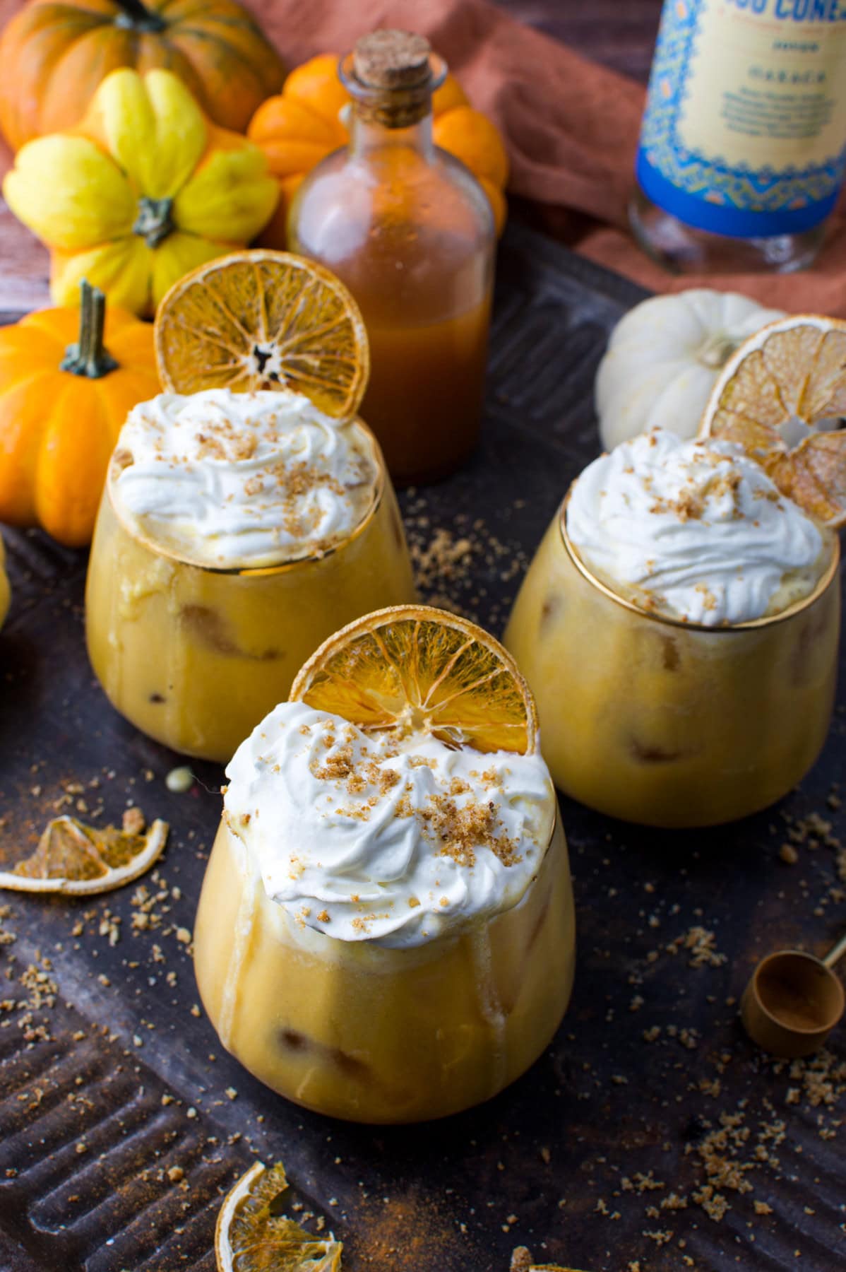 Creamy Pumpkin Pie Spiced Mezcal Cocktail topped with whipped cream and dried orange slices. Perfect for fall-inspired, holistic living.