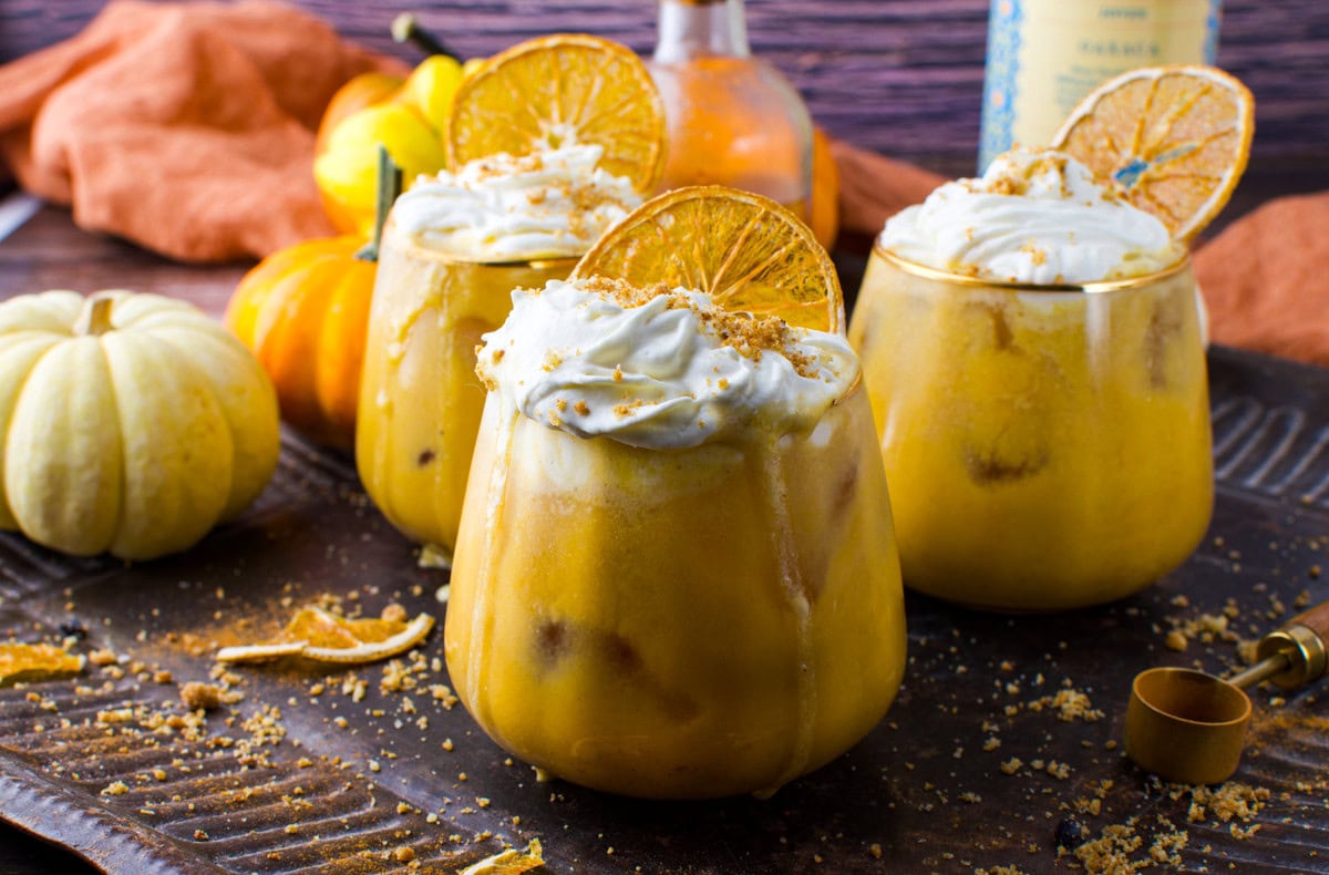 Creamy pumpkin spice smoothies garnished with whipped cream and dried orange slices, perfect for fall.