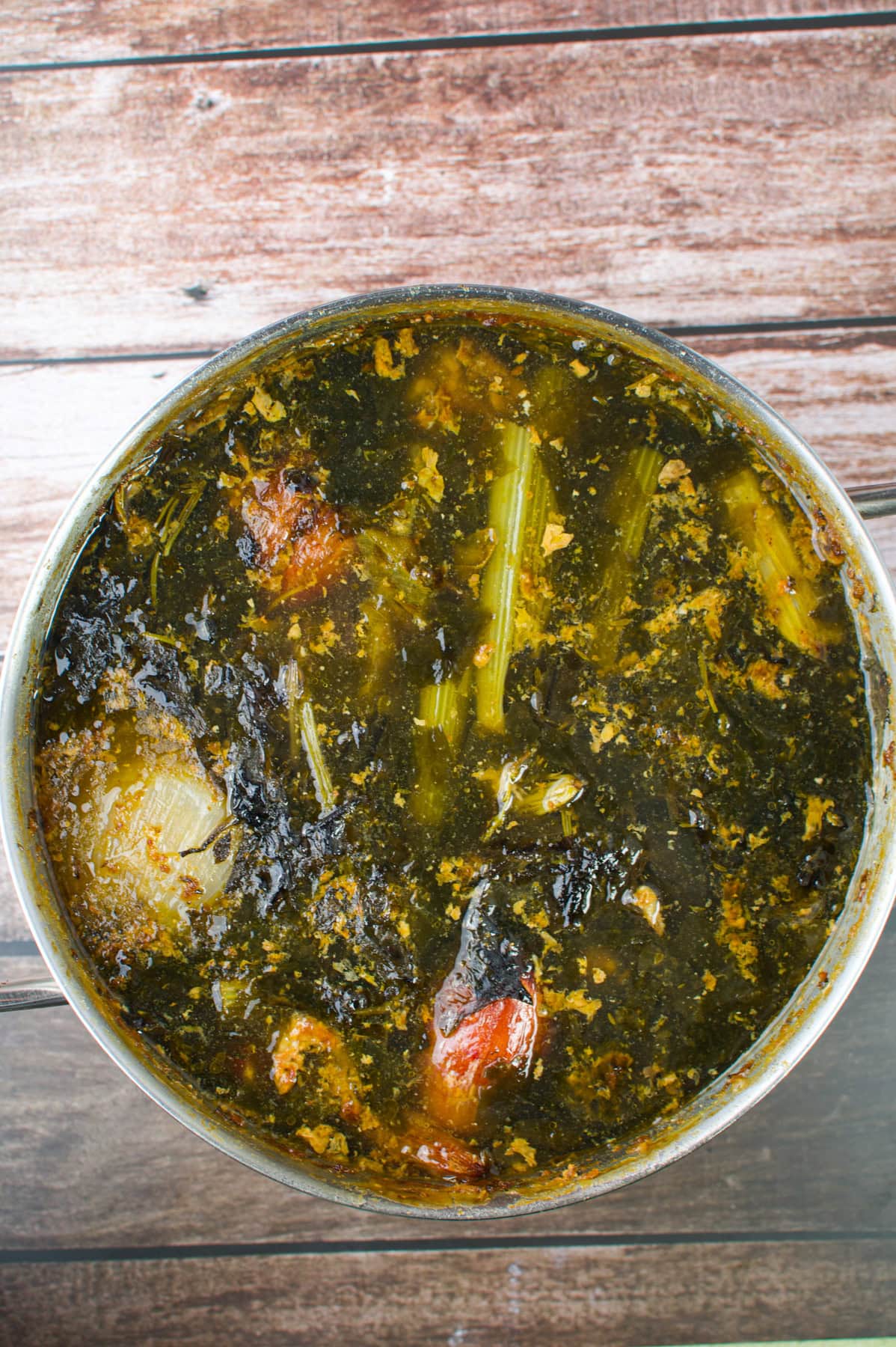 A bowl of Nigerian afang soup with leafy greens, meat, and pieces of stockfish, placed on a wooden surface.
