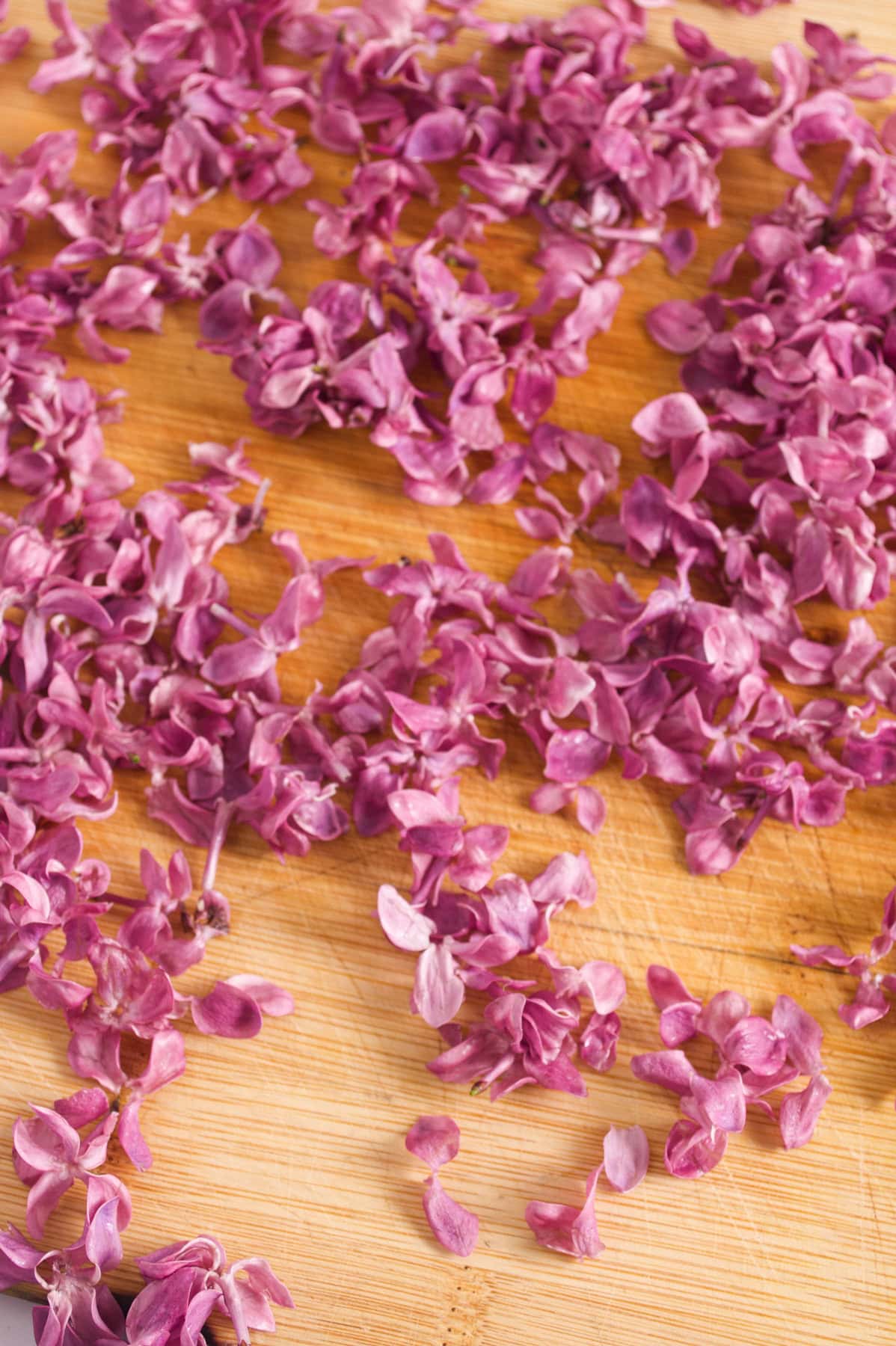 Purple flower petals scattered across a wooden surface, creating a natural and vibrant pattern with a mix of small and larger petal clusters.
