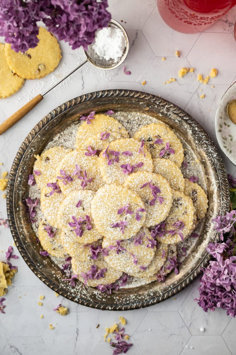 Lilac butter cookies on a silver plate with lilac blossoms on the table.