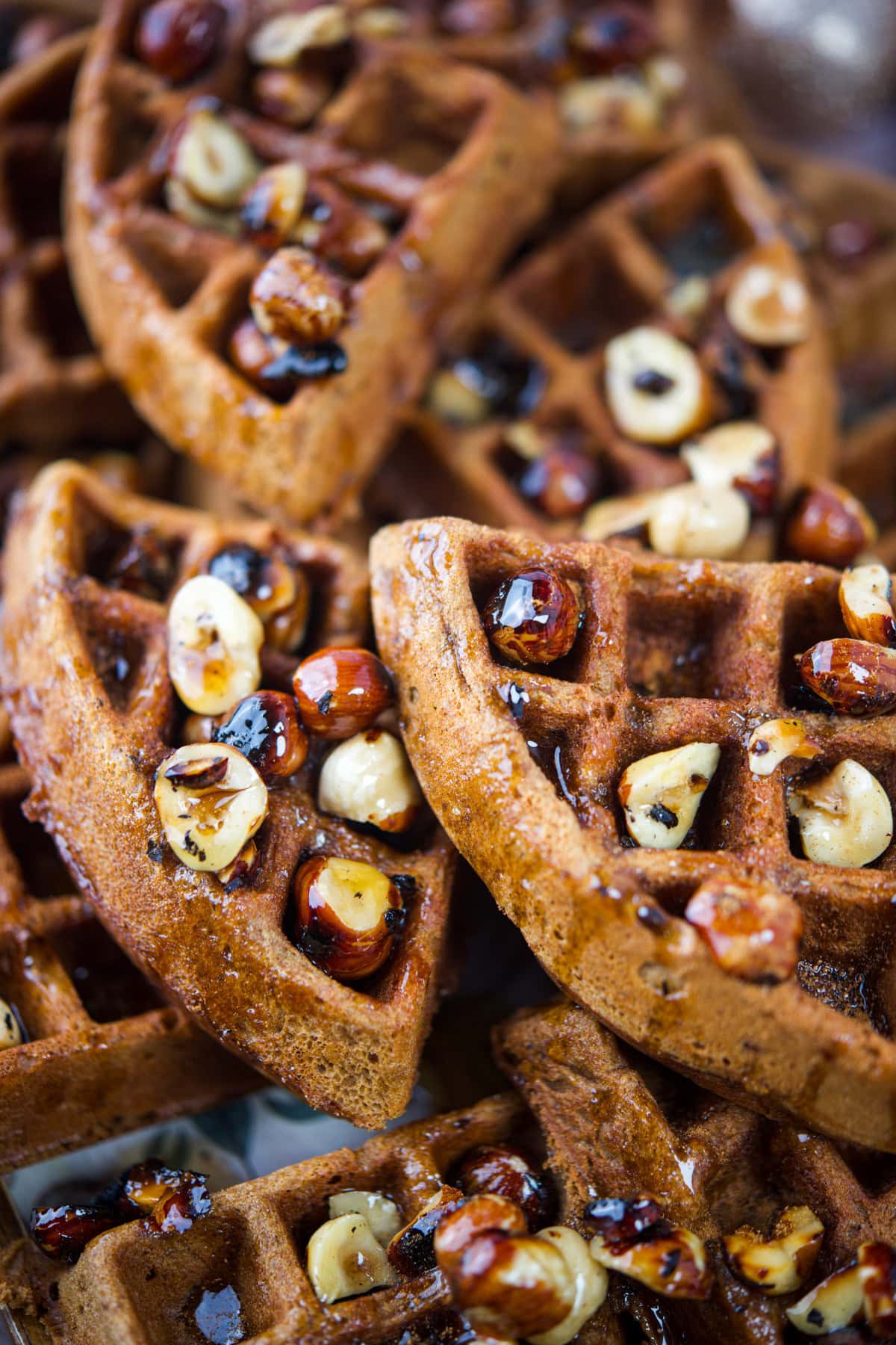 Close-up of Gingerbread Waffles (Gluten-Free) topped with roasted hazelnuts and drizzled with syrup, showing a crisp texture and a glossy finish on the nuts.