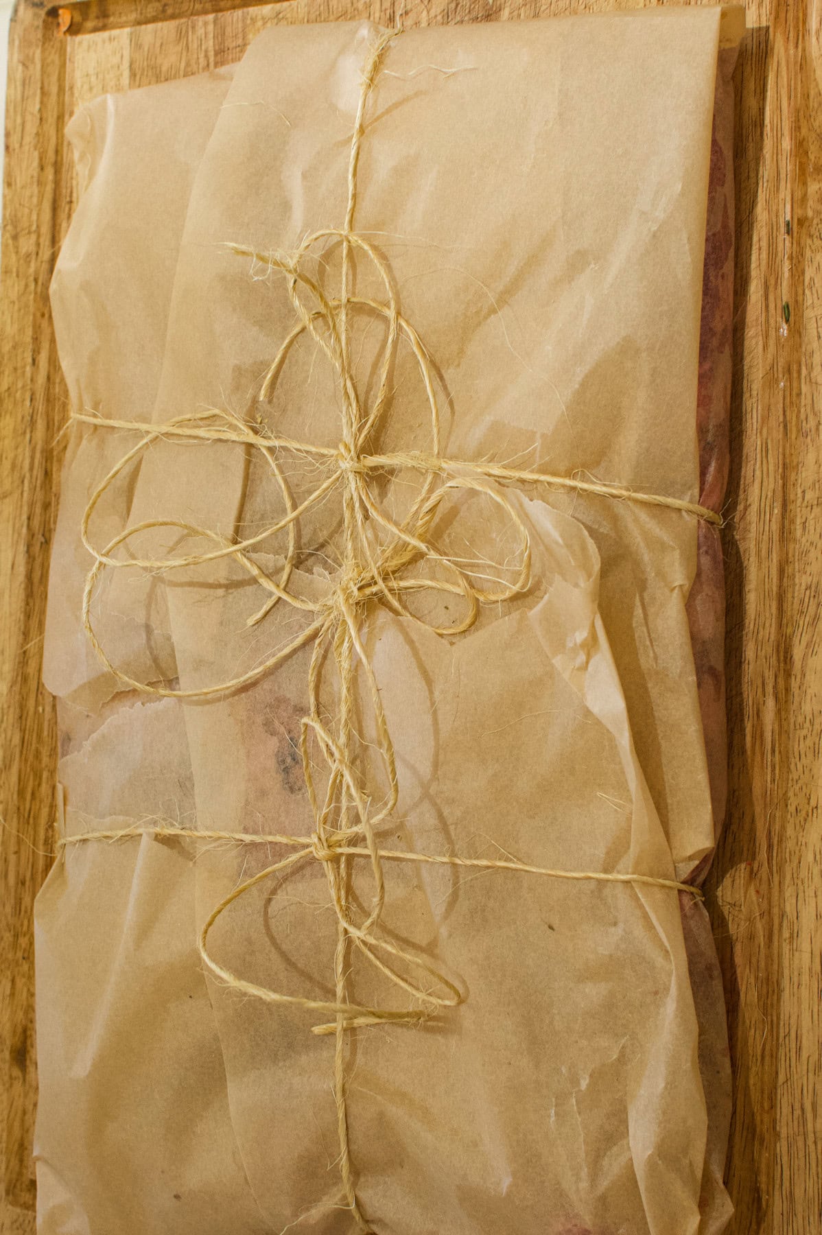 A rectangular object wrapped in brown parchment paper and tied with a thin piece of twine, resting on a wooden surface.