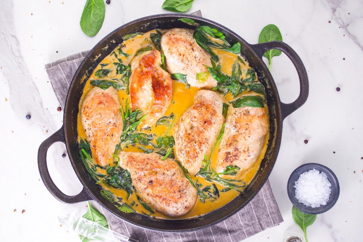 Juicy chicken breasts cooking in a skillet with spinach and a creamy sauce.