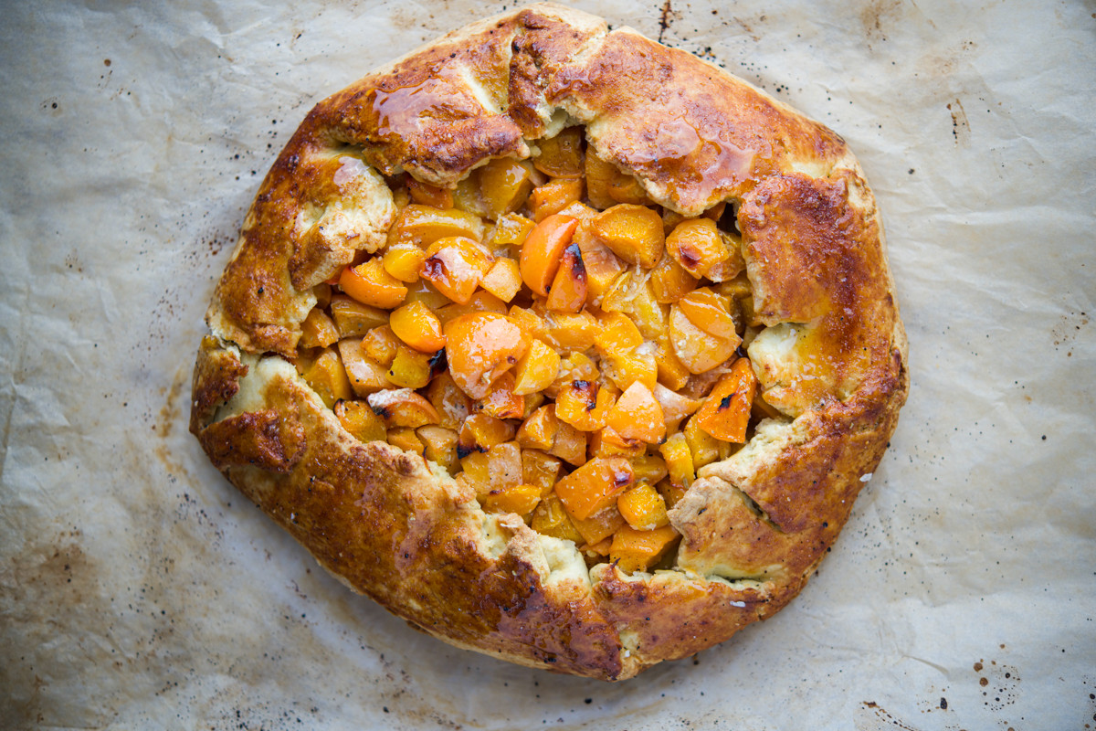 A rustic apricot galette with a golden, flaky crust and a filling of chopped apricots sits on parchment paper, baked to perfection and glistening with a light glaze.