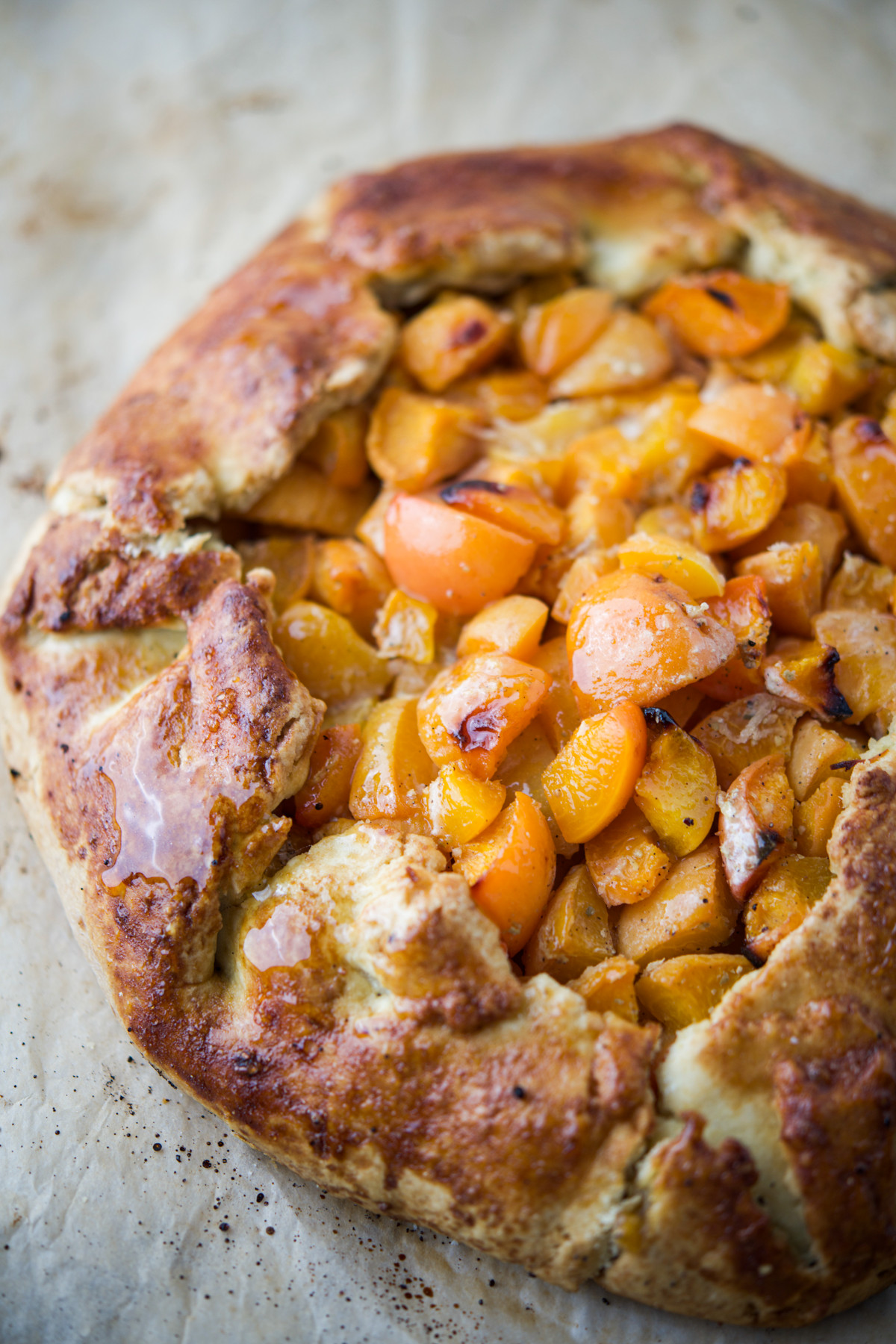 A rustic apricot galette with a golden, flaky crust, filled with sliced, juicy apricots, sits on a piece of parchment paper.