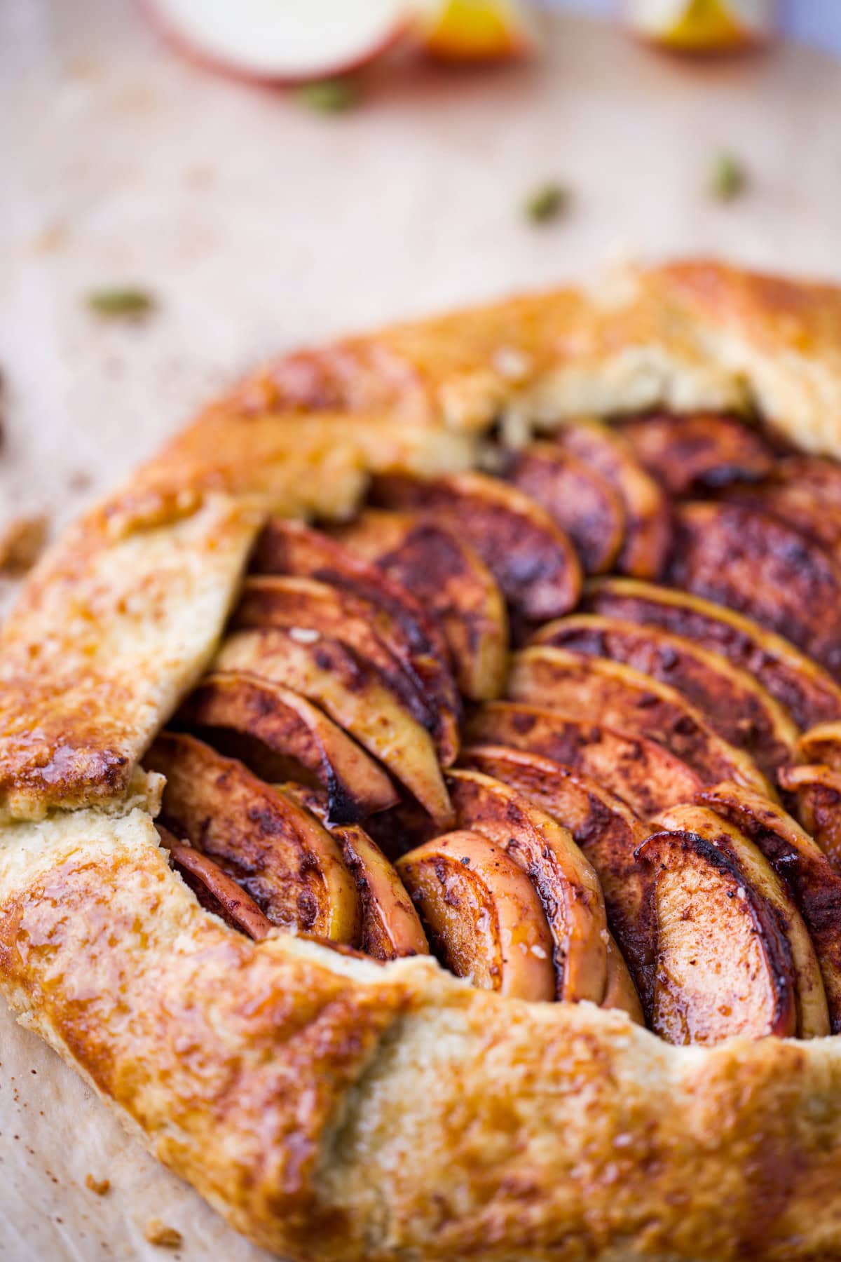 A close-up of a rustic apple galette with golden, flaky crust and spiced apple slices arranged neatly inside, resting on parchment paper.