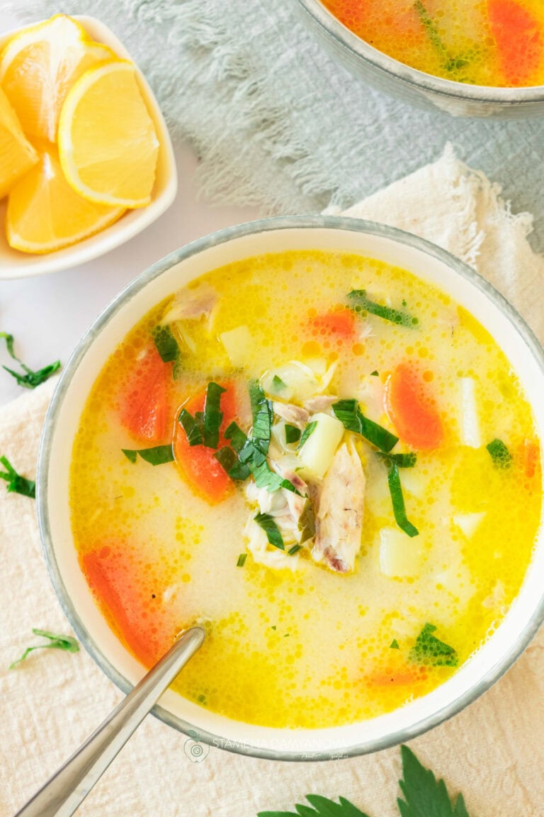 Bowl of Greek fish soup (Avgolemono) with chunks of white fish, vegetables, and a creamy lemon-egg broth, garnished with fresh dill and lemon slices, served with rustic bread on the side.