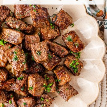 A scalloped plate filled with browned air fryer steak bites, garnished with chopped herbs. A banner at the top reads Air Fryer Steak Bites and a footer at the bottom displays thetastesoflife.com.