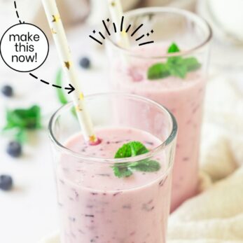 Two tall glasses of blueberry smoothie with straws and mint leaves on top. Fresh blueberries are scattered around on a light-colored surface. Text on the image reads, “Healthy Blueberry Smoothie,” and “easy to make • incredible taste.”.
